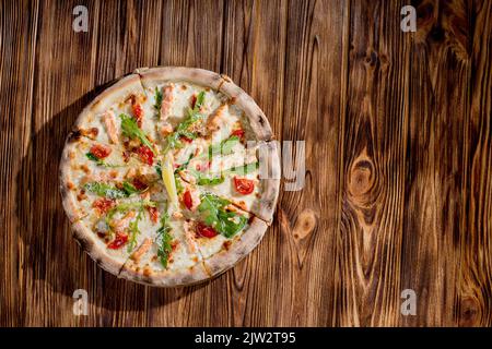 Pizza mit Lachs, Mozzarella, Kirschtomaten, Rucola, Zitrone und Parmesan. Italienische Küche auf einem woden Hintergrund. Stockfoto