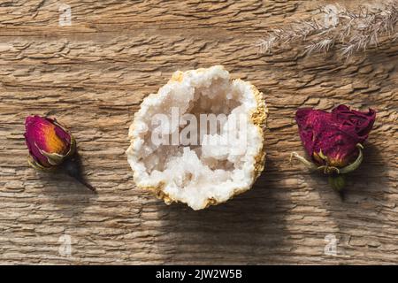 Quarz aus Geode-Mineralstein mit trockenen Rosen auf Holzgrund Stockfoto