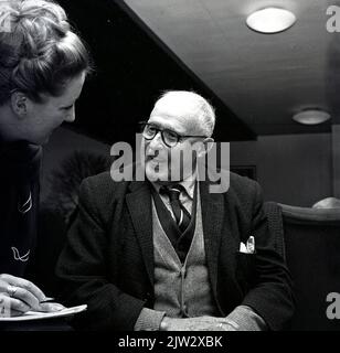 1965, ein historischer, gut gekleideter älterer Mann, der eine Jacke und Krawatte sowie zwei Strickjacken trägt, wurde von einer Journalistin in einem Altersheim in Schottland, Großbritannien, interviewt. Stockfoto