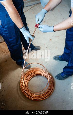 Installationsarbeiten. Zwei Männer in blauen Overalls und Schutzhandschuhen bereiten Fußbodenheizung für die Wasserheizung auf der Baustelle vor. Baugewerbe Stockfoto