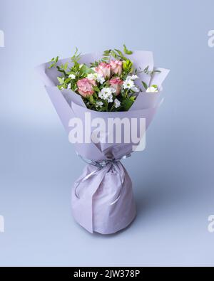 Zartes Rosenstrauß, umhüllt von hellem Blumenpapier, steht auf blauem Hintergrund. Schön verpacktes Blumenarrangement mit rosa Rosen, weiß c Stockfoto