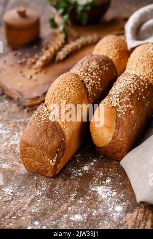 Nahaufnahme von Mehrkornbrötchen auf einem Holztisch im rustikalen Stil. Brotprodukte mit Sesam auf unscharfem rustikalem Hintergrund mit Dornen. Gebäck und Stockfoto