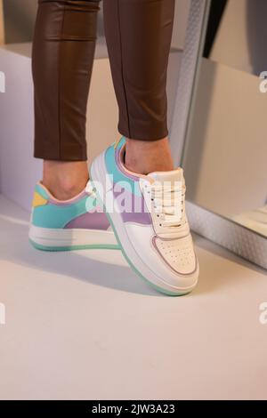 Nahaufnahme von modisch farbigen Sneakers auf den Beinen eines Teenagers. Mädchen in braunen Hosen steht durch Spiegel zeigt eine neue Kollektion von laceup sp Stockfoto