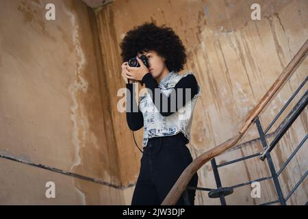 Frau mit gemischter Rasse, die mit der Kamera auf einer Treppe fotografiert Stockfoto