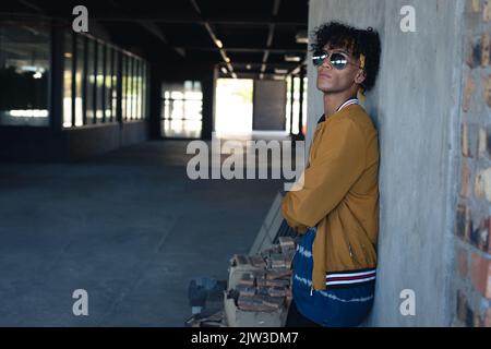 Gemischter Renner in leerem Gebäude, der eine Sonnenbrille trägt und wegschaut Stockfoto