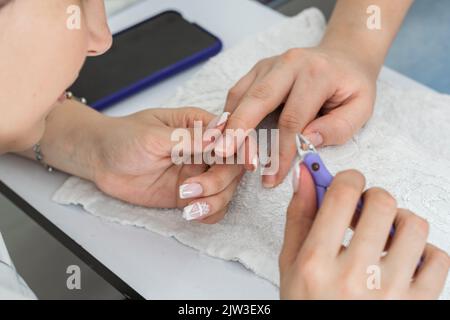 Detailaufnahme der Hände eines lateinischen Manikuristen, der die richtige Reinigung der Nägel mit einer Zange oder einer Nagelhautschere durchführt, vorsichtig abstumpsen Stockfoto