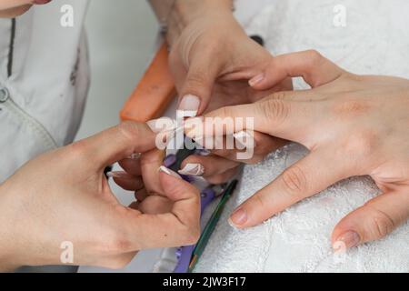 latina Manikuristin macht die jeweilige Messung der Nägel, mit falschen Nägeln misst sie genau, wo das Gel aufgetragen werden sollte Stockfoto