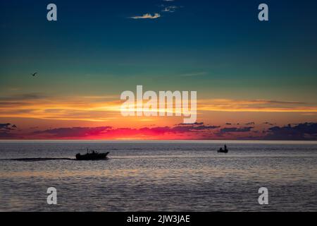 Die Morgensonne steht kurz vor dem Aufgehen hinter den Fischern in ihren Booten auf dem Lake Michigan vor der Küste von Manitowoc, Wisconsin. Stockfoto