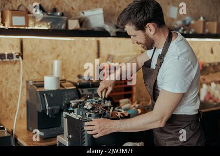 Lächelnder junger Mann, der in einer Werkstatt die Kaffeemaschine repariert Stockfoto