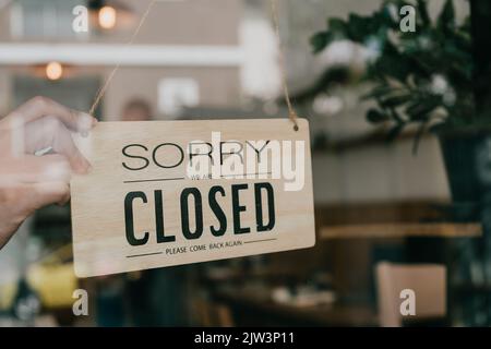 Das Schild für das Business Coffee Cafe Shop hängt an der Tür und zeigt einen Laden in der Nähe mit einem Café und Restaurant, das im Bokeh-Hintergrund verwischt. Stockfoto