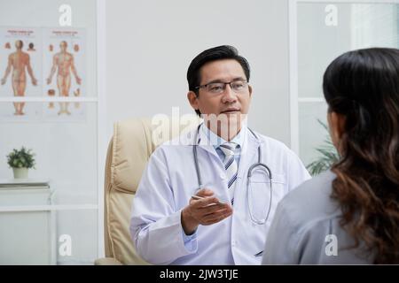 Erfahrener vietnamesischer Arzt, der eine Patientin in seinem Büro konsultiert Stockfoto