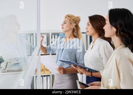 Multiethnische Geschäftsfrauen schreiben Ideen auf Glaswand Stockfoto