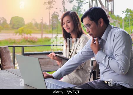 Asiatische Geschäftsfrauen tauschen sich mit Kollegen außerhalb des Büros mit Notebooks in einer lustigen Atmosphäre aus. Stockfoto