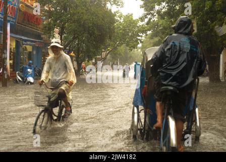 Monsun regnet in der Stadt Hue. Die Menschen in Tuc-Tuc fahren Fahrrad entlang überfluteter Straßen in Hue. Vietnam. Überschwemmungen. Ein Großteil Indiens steht vor einer Zunahme Stockfoto