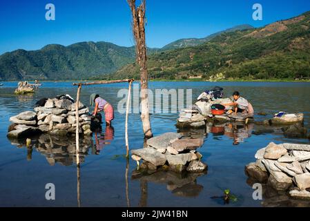 Frau wäscht Kleidung in Largo Atitlan, Santiago de Atitlan, Guatemala. Verschmutzte Seen. Das Wasser des Atitlán-Sees wird aufgrund des Aussehens von A grün Stockfoto