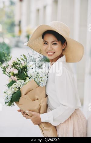 Attraktive lächelnde junge Frau in Strohhut mit Sommerstrauß Stockfoto