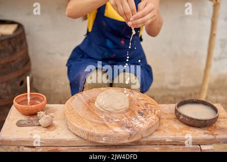 Die Handwerkerin webt ihre Hände in eine Schüssel mit Wasser, um Ton zu bilden Stockfoto