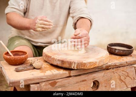 Potter männlicher Meister in hellem Leinenhemd mit nassem Tontopf in den Händen. Töpferei Hobby Mann Hände Formen in Ton Stockfoto