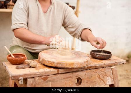 Männlicher Meister in einem hellen Leinenhemd zeigt, wie man im Meisterkurs aus Lehm Formen kann Stockfoto