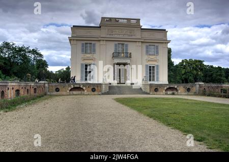 Paris, Frankreich - 29. Mai 2022: Blick auf die Vorderseite des Chateau de Bagatelle über einen reich verzierten Garten mit Bäumen, Rasen, Hecke und Touristen Stockfoto