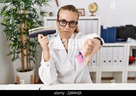 Junge kaukasische Frau mit Zahnaufhellung Palette unglücklich und wütend, Ablehnung und negativ mit Daumen nach unten Geste. Bad expressio Stockfoto