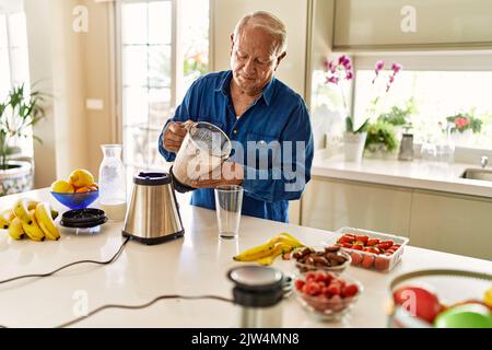 Älterer Mann, der in der Küche Smoothie auf Glas gießt Stockfoto