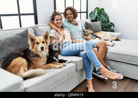 Mann und Frau Paar lächeln selbstbewusst und umarmen sich, sitzen auf dem Sofa mit Hunden zu Hause Stockfoto