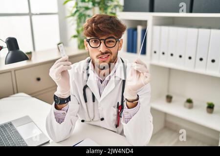 Arabischer Arzt Mann mit Bart hält covid Test ahnungslos und verwirrt Ausdruck. Zweifel Konzept. Stockfoto