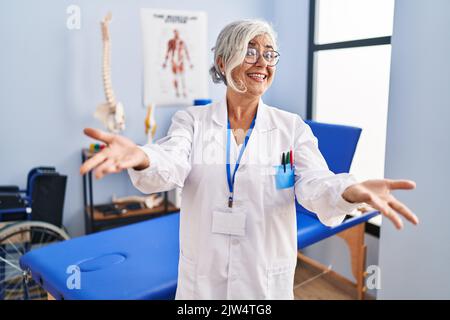 Frau im mittleren Alter mit grauen Haaren, die in der Schmerzheilungsklinik arbeitet, lächelt fröhlich und bietet ihnen die Hände an, die Hilfe und Akzeptanz geben. Stockfoto