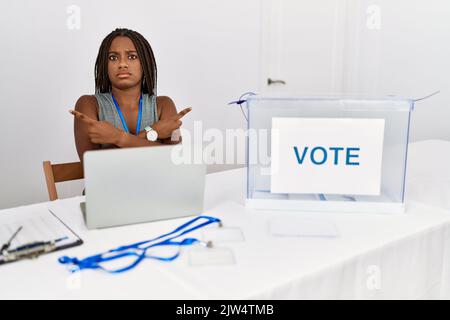 Junge afroamerikanische Frau, die bei den politischen Wahlen arbeitet, bei der Wahl auf beiden Seiten mit den Fingern sitzend, unterschiedliche Richtungen sind nicht einig Stockfoto