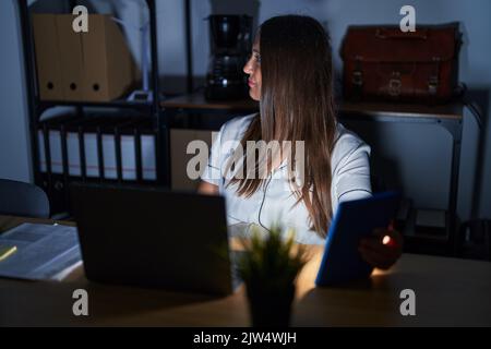 Junge Brünette Frau arbeitet im Büro in der Nacht Blick zur Seite, entspannen Profil Pose mit natürlichem Gesicht und selbstbewusstes Lächeln. Stockfoto
