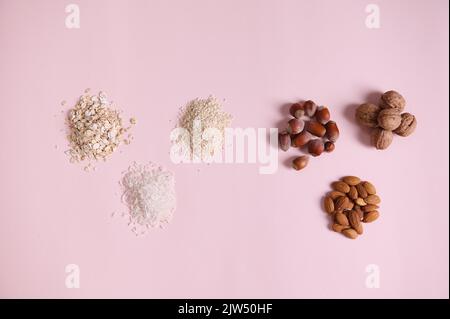 Flaches Stillleben mit einer Auswahl an gesunden Bio-Rohsamen, Nüssen und Bohnen auf rosa Hintergrund isoliert Stockfoto
