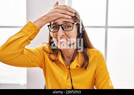 Junge Frau mit Headset für Callcenter-Agenten gestresst und frustriert, mit der Hand am Kopf, überrascht und ärgerlich im Gesicht Stockfoto