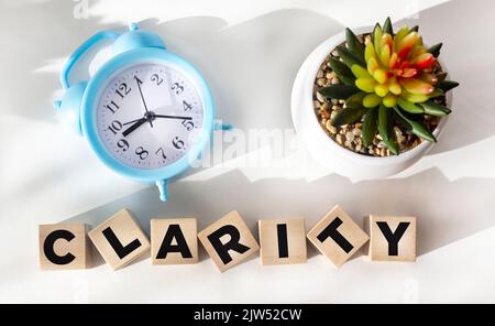 Klarheit Wort auf Holzblock und weißem Hintergrund mit Uhr und Kaktusblüte geschrieben. Stockfoto