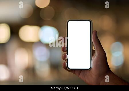 Männliche Hand hält Smartphone mit weißem Bildschirm auf Nacht Stadt Hintergrund. Stockfoto