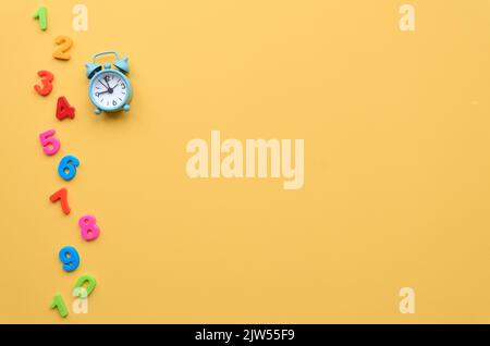 Kleiner Wecker und Figuren auf gelbem Hintergrund, flach liegend, Draufsicht. Stockfoto