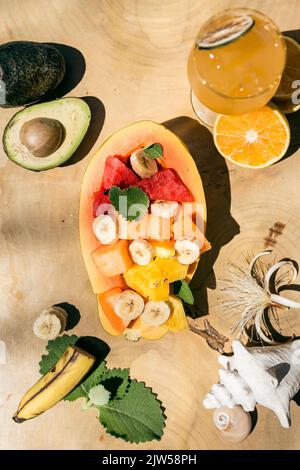 Obst wird in einer Papaya serviert. Banane, Wassermelone, Melone, Ananas, Avocado und Orange. Natürlicher Orangensaft, serviert in einem Glasbecher. Szene eingestellt von Stockfoto