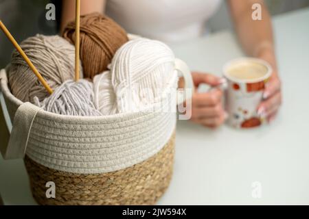 Frauen Hobby Stricken. Pastellfarbenes Garn im Korb auf weißem Tisch. Stockfoto