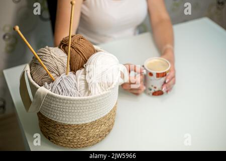 Frauen Hobby Stricken. Pastellfarbenes Garn im Korb auf weißem Tisch. Stockfoto