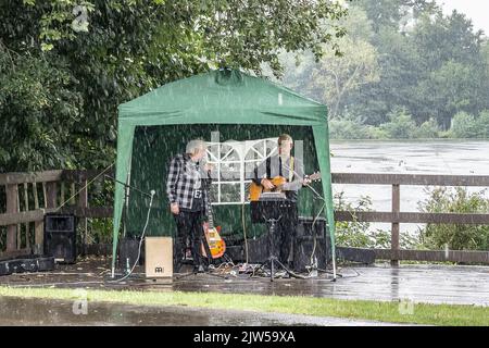 Kidderminster, Großbritannien. 3.. September 2022. Britisches Wetter: Scharfe und schwere Regenschauer trafen heute die Midlands, aber wenn Darsteller eine Aufführung für wohltätige Zwecke in einem lokalen Landschaftspark versprochen haben, geht die Show immer noch weiter. Graham und Bobby sind hier, um den Klassiker von Everly Brothers „Crying in the Rain“ zu erleben, während sich der Himmel öffnet! Kredit: Lee Hudson/Alamy Live Nachrichten Stockfoto