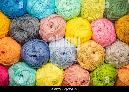 Hintergrund aus farbigem Garn. Nahaufnahme der Fadenkugeln. Materialien für Nadelarbeit. Rack mit Garn im Laden. Regal mit mehrfarbigem Gewinde für kn Stockfoto