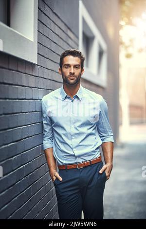 Setzen Sie sich Ihre eigenen Ziele. Porträt eines hübschen jungen Geschäftsmannes, der gegen eine graue Backsteinmauer steht. Stockfoto