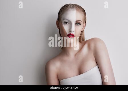 Eine schöne Frau trägt Gesichtsfarbe und roten Lippenstift vor einem schlichten Hintergrund. Stockfoto