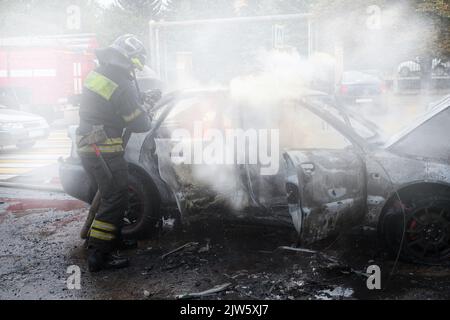 Die Feuerwehr löscht ein brennendes Auto. Brandstiftung eines Autos in der Stadt. Stockfoto