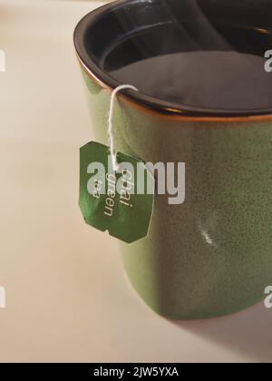 Nahaufnahme einer grünen Tasse Chai grünen Tee mit Anhänger über der Seite hängen. Stockfoto