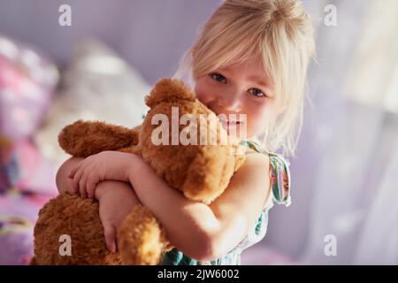 Hält sich fest an ihren flauschigsten kleinen Freund. Porträt eines entzückenden kleinen Mädchens, das einen Teddybären umarmt. Stockfoto