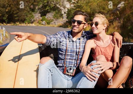 Gehen Sie einfach auf einen Roadtrip und entdecken Sie die Schönheit. Ein junger Mann zeigt auf etwas, während auf einem Roadtrip mit seiner Freundin. Stockfoto