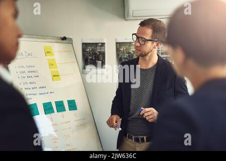 Im Gespräch mit dem Team durch seinen Vorschlag. Ein junger Mann, der eine Präsentation vor Kollegen in einem Büro gibt. Stockfoto