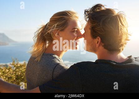 Die Sonne scheint und Sie auch. Ein liebevolles Paar sitzt auf einer Bank mit Blick auf das Meer. Stockfoto