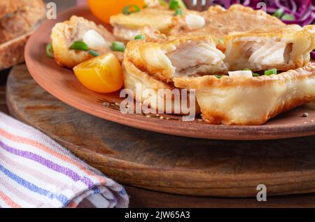 Vorne, Nahansicht von mehreren Tilapia-Stücken, die mit gelben Kirschtomaten, Rotkohl auf runder Steinware auf Holztisch, rustikal, selecti zerschlagen wurden Stockfoto